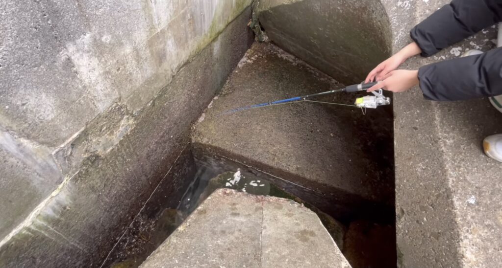 カサゴが釣れるテトラ帯の穴釣りの様子。短い竿でテトラポットの隙間に仕掛けを落として根魚を狙う、カサゴ釣りの実践シーン